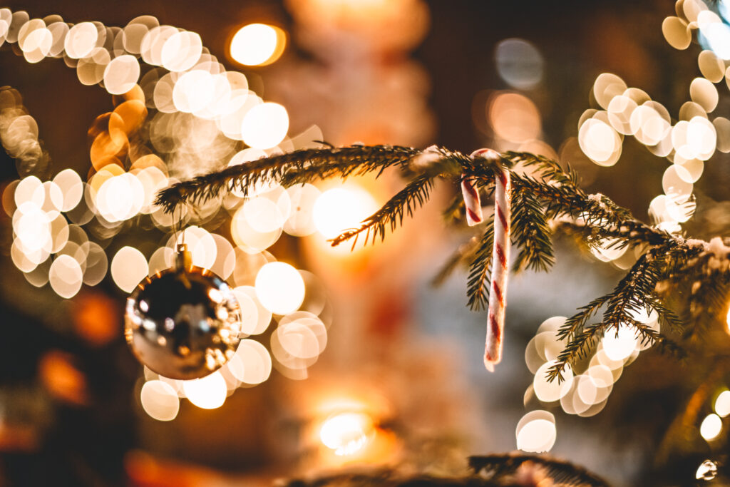 kultainen joulupallo ja karamellitanko roikkumassa joulukuusen oksalla, taustalla jouluvaloja